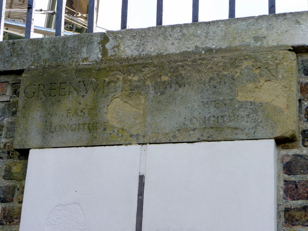 ป้ายหินสลักคำว่า Greenwich Meridian แบ่งฝั่ง East Longitude และ West Longitude มีแถบโลหะแนวตั้งตรงกลาง