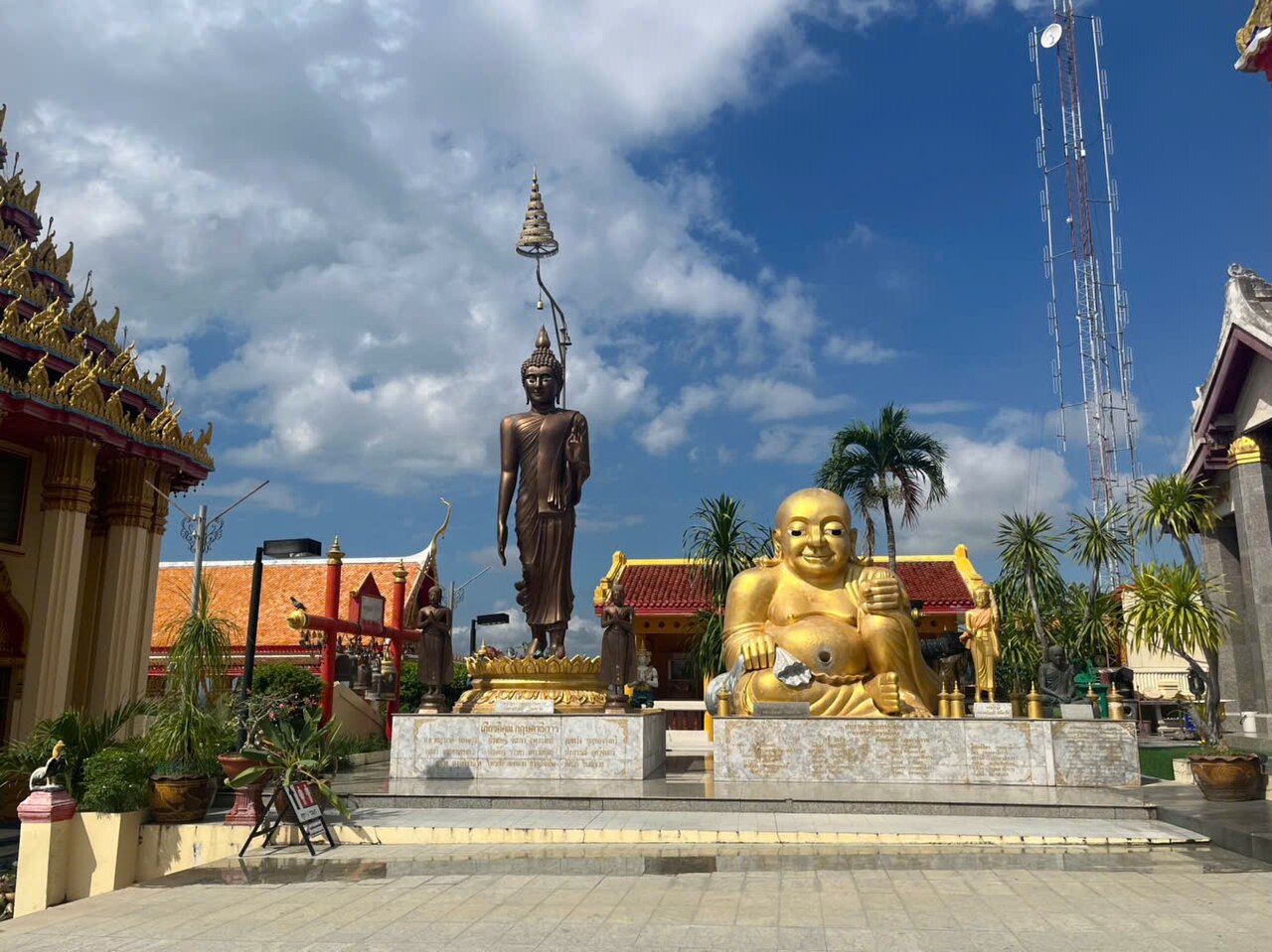 ลานวัดบนเขาสะแกกรัง มีพระพุทธรูปยืนสีสำริดและรูปเคารพสีทอง ท้องฟ้าสีฟ้ามีเมฆ