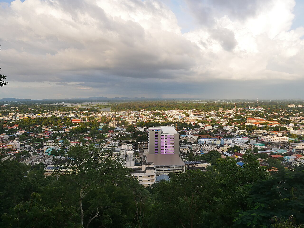 ทิวทัศน์ตัวเมืองอุทัยธานีมองจากที่สูง มีต้นไม้ด้านหน้าและเมฆฝนบนท้องฟ้า