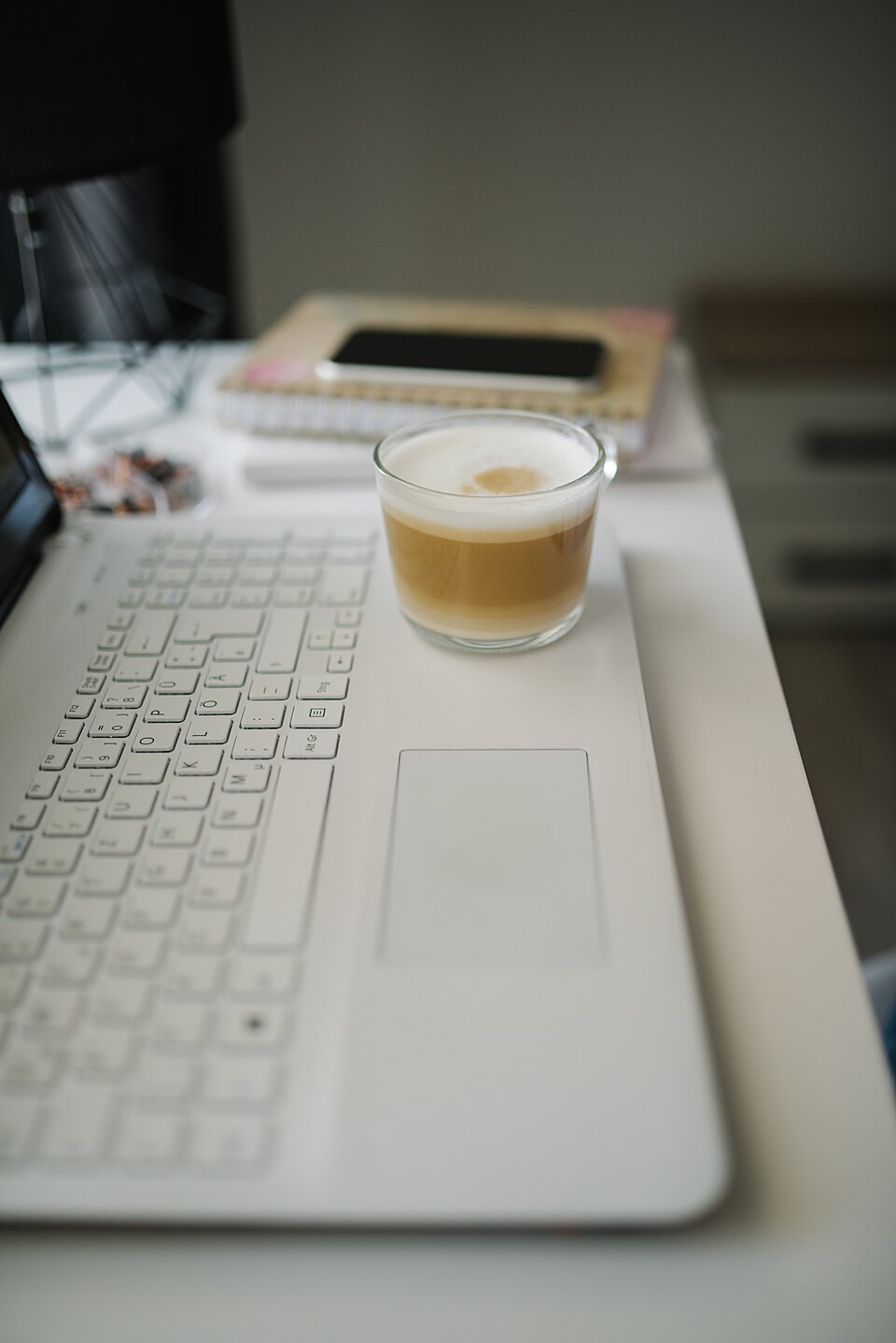 แก้วกาแฟวางบนโต๊ะทำงานพร้อมโน้ตบุ๊กและสมุดจด