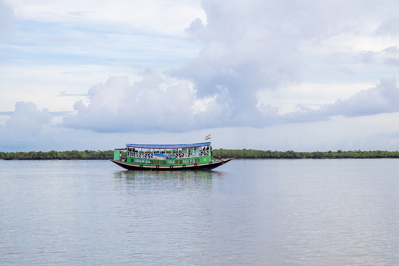 เรือนำเที่ยวสองชั้นลอยอยู่กลางลำน้ำกว้าง มีแนวป่าชายเลนเป็นเส้นยาวอยู่ไกล ๆ